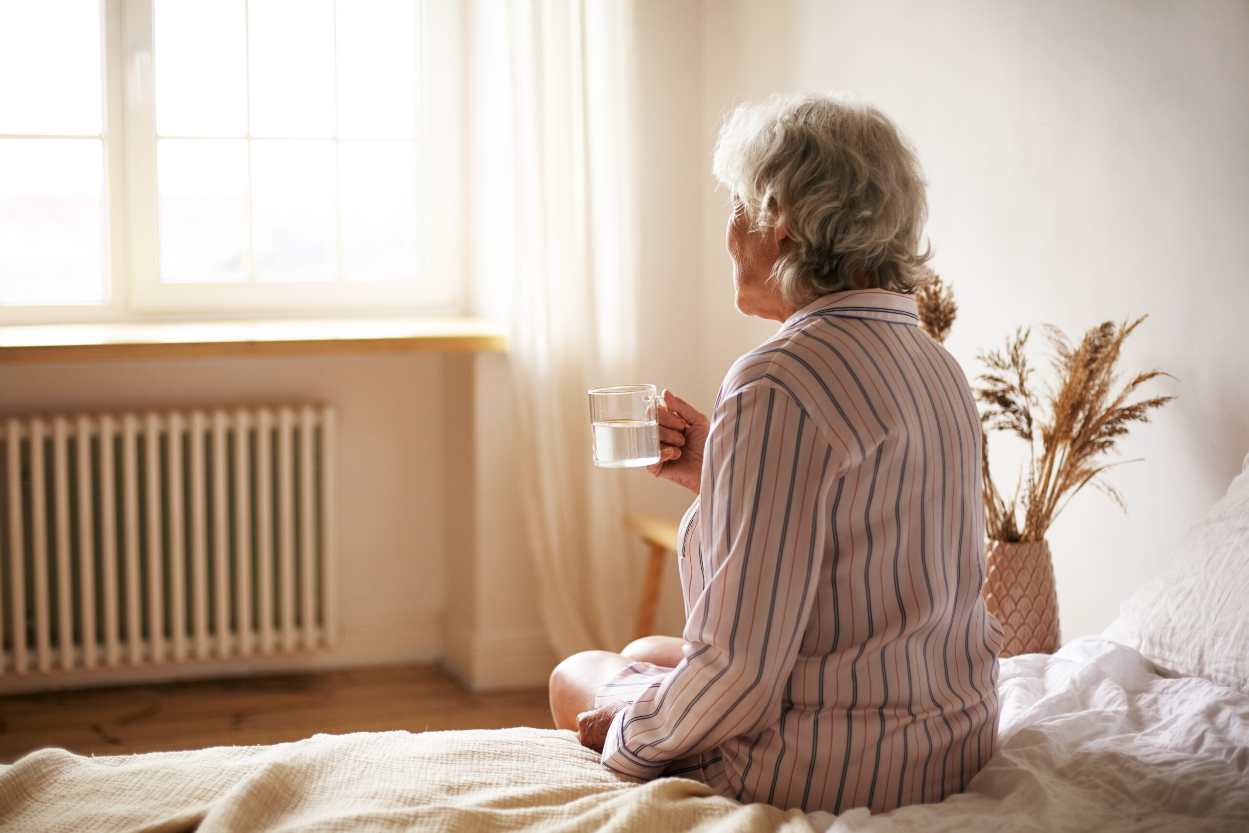 rear view senior sixty year old woman with gray hair holding mug washing down sleeping pill suffering from insomnia elderly retired female taking medicine with water sitting bedroom scaled 1