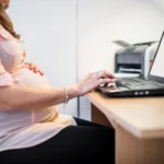 midsection view pregnant woman using laptop wooden desk