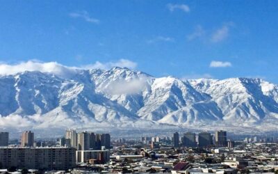Vista da cidade de Santiago, no Chile, com prédios em primeiro plano e a Cordilheira dos Andes coberta de neve ao fundo, sob céu azul