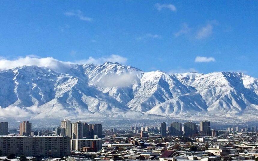 Vista da cidade de Santiago, no Chile, com prédios em primeiro plano e a Cordilheira dos Andes coberta de neve ao fundo, sob céu azul